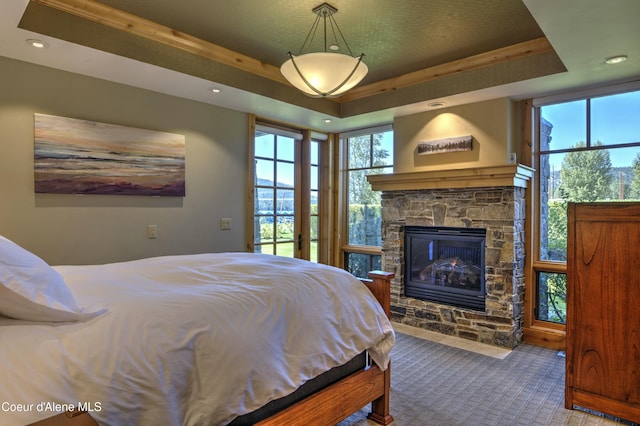 carpeted bedroom featuring recessed lighting, a raised ceiling, multiple windows, and a fireplace