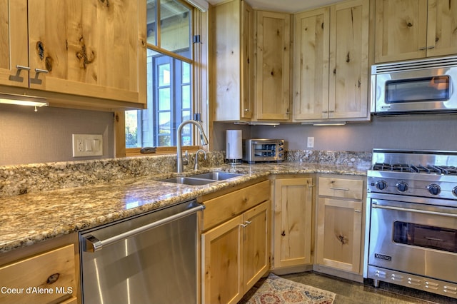 kitchen with appliances with stainless steel finishes, a sink, light stone counters, and light brown cabinetry