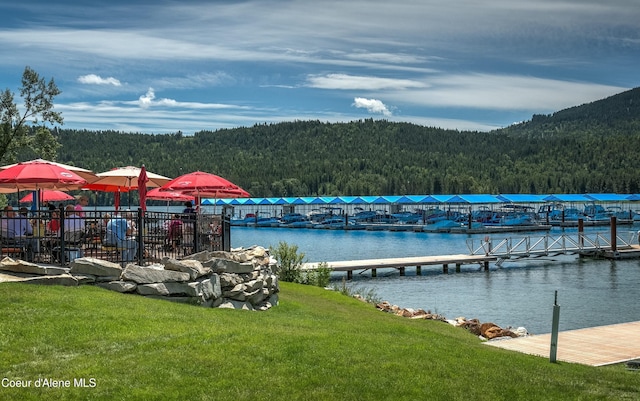 view of dock with a forest view, a lawn, and a water view