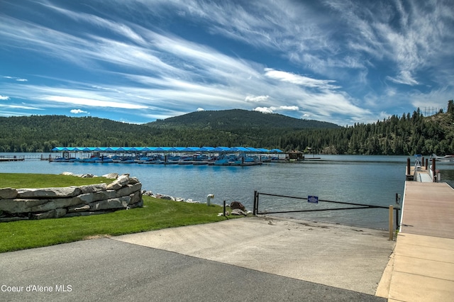 view of water feature with a forest view, a dock, and a mountain view