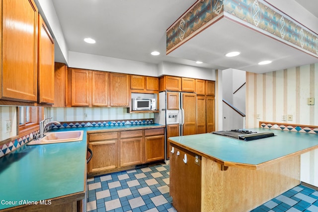 kitchen with a breakfast bar, dark floors, brown cabinets, a sink, and wallpapered walls