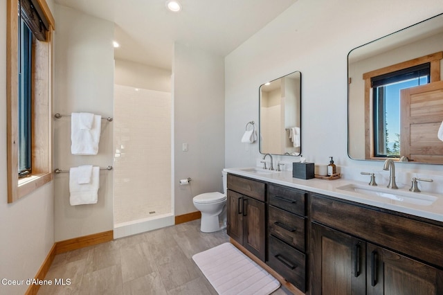 bathroom with toilet, baseboards, a tile shower, and a sink