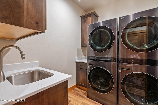 laundry room featuring stacked washer and clothes dryer, cabinet space, a sink, and light wood-style flooring