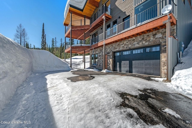 snow covered property with an attached garage and stone siding