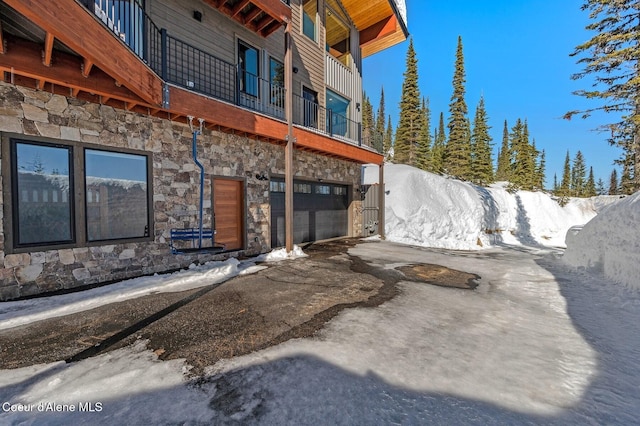 view of snow covered exterior with stone siding, driveway, and an attached garage