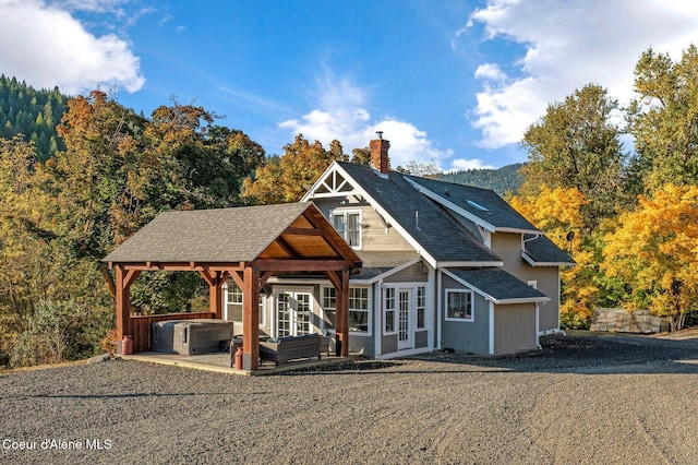 view of front of house featuring a chimney, roof with shingles, and a hot tub