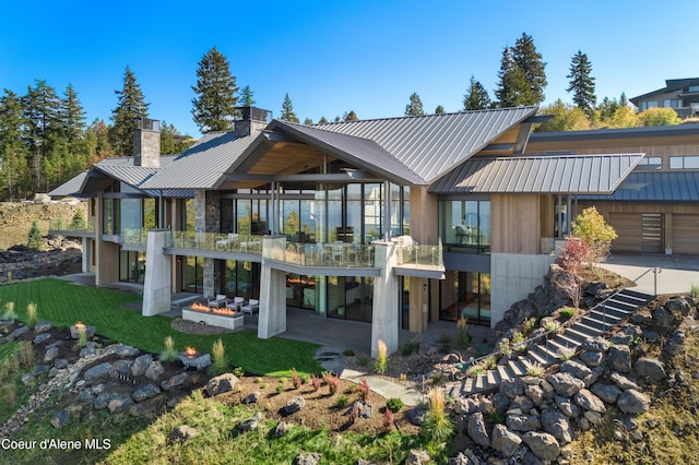 rear view of property with a chimney, concrete driveway, a standing seam roof, a patio area, and metal roof