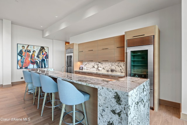 kitchen with light wood-type flooring, modern cabinets, high end refrigerator, and a kitchen breakfast bar