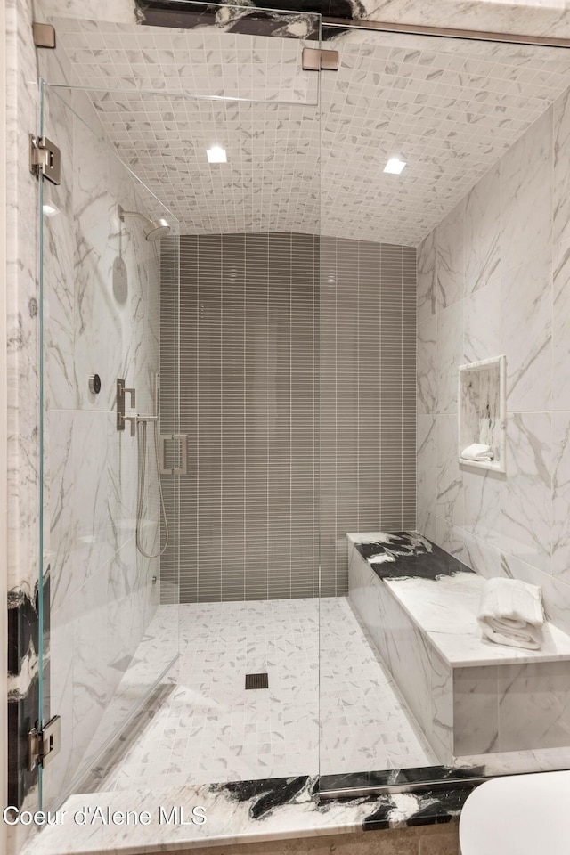 bathroom with toilet, a marble finish shower, and tile walls