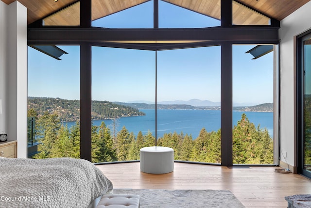 unfurnished bedroom featuring lofted ceiling, a water and mountain view, a view of trees, wood finished floors, and a wall of windows