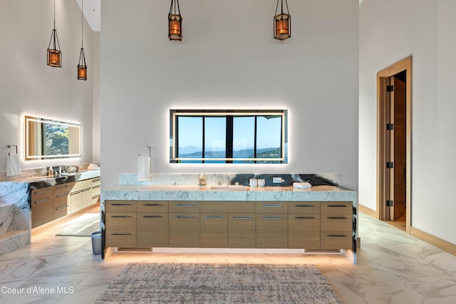 kitchen with marble finish floor, modern cabinets, a towering ceiling, and decorative light fixtures