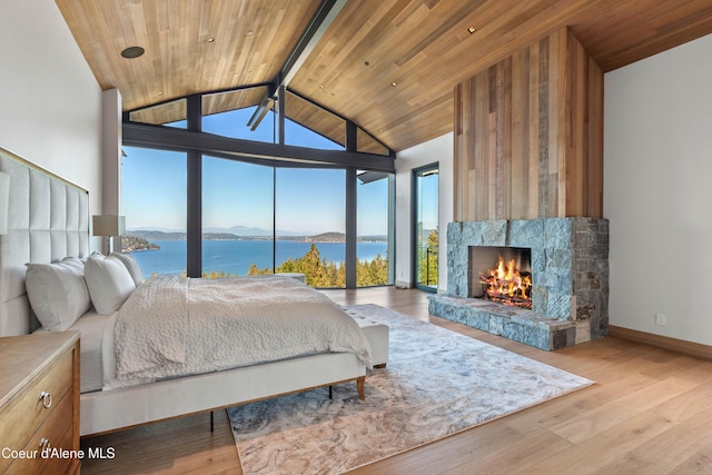 bedroom featuring baseboards, wooden ceiling, a water view, a lit fireplace, and light wood-style floors