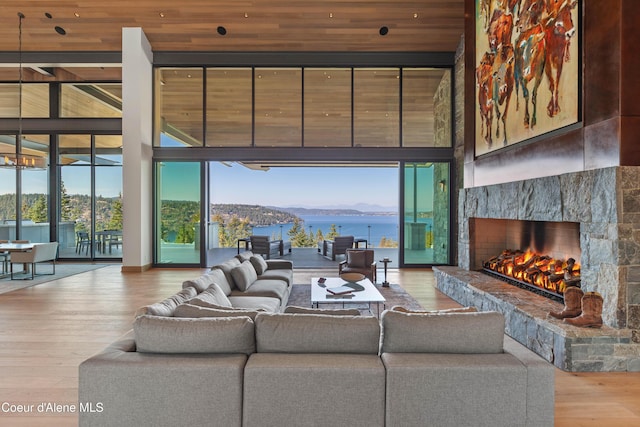 living room with light wood finished floors, a towering ceiling, a premium fireplace, a water and mountain view, and a wall of windows