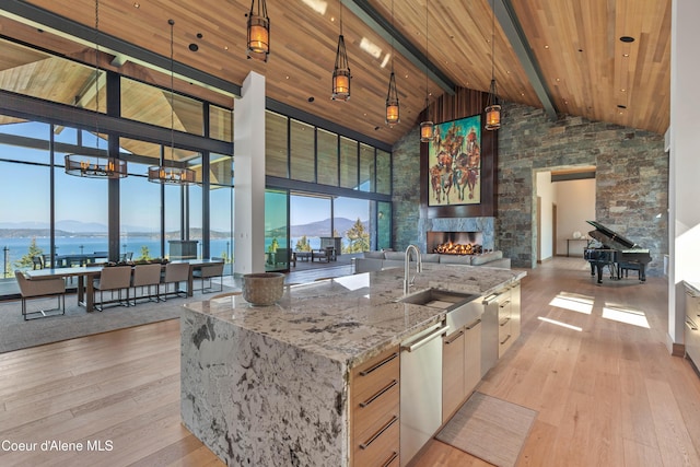 kitchen featuring a kitchen island with sink, light stone counters, a water and mountain view, and pendant lighting