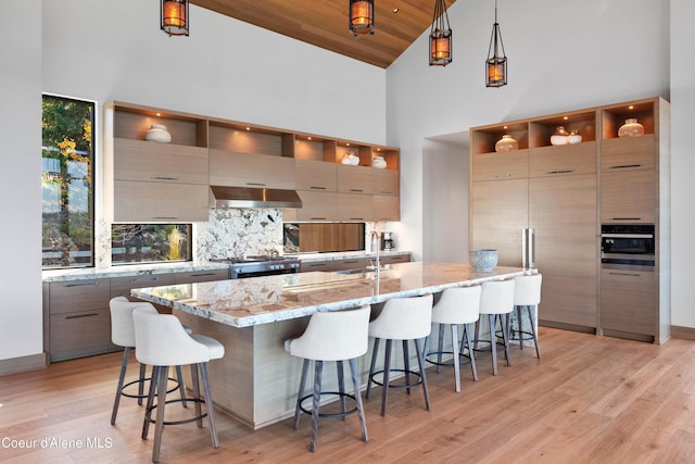 kitchen with hanging light fixtures, modern cabinets, light stone counters, and an island with sink