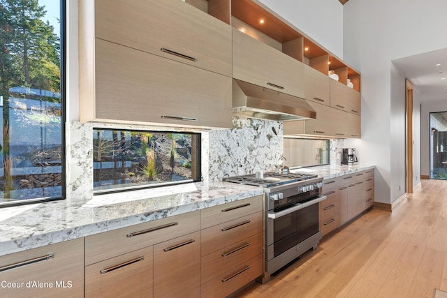 kitchen with exhaust hood, double oven range, light stone countertops, light wood finished floors, and tasteful backsplash