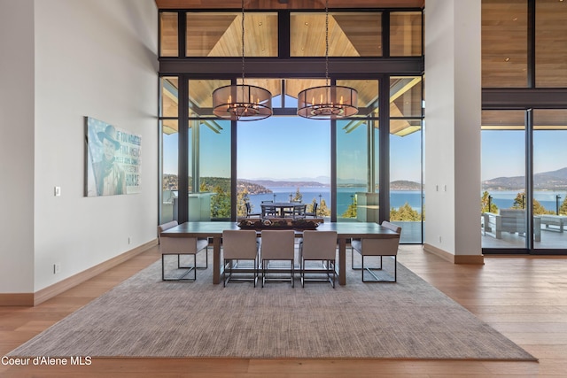 dining room with a notable chandelier, wood finished floors, baseboards, a water and mountain view, and a wall of windows