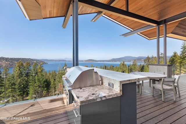 wooden terrace with an outdoor bar, a water and mountain view, and area for grilling