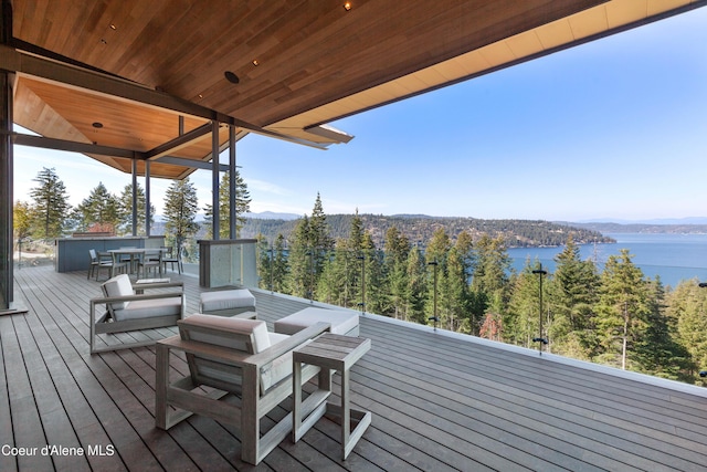 deck featuring a water view, outdoor dining area, and a view of trees