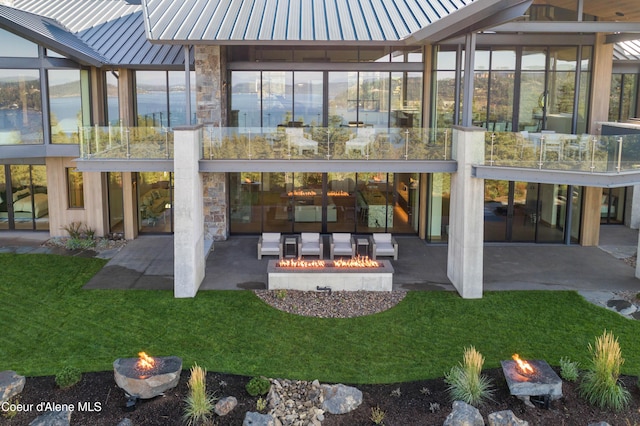 back of house featuring a patio, an outdoor fire pit, a standing seam roof, metal roof, and stone siding