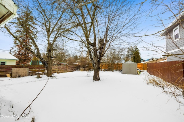 snowy yard with an outbuilding, fence, and a storage shed