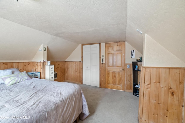 bedroom featuring a wainscoted wall, light colored carpet, vaulted ceiling, wood walls, and a textured ceiling