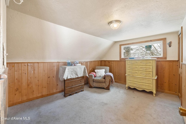 sitting room with a textured ceiling, wood walls, lofted ceiling, and a wainscoted wall