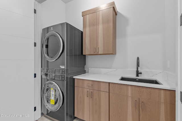 clothes washing area featuring stacked washer / dryer, cabinet space, and a sink