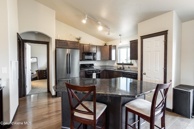 kitchen featuring lofted ceiling, dark brown cabinetry, a sink, black appliances, and a kitchen bar