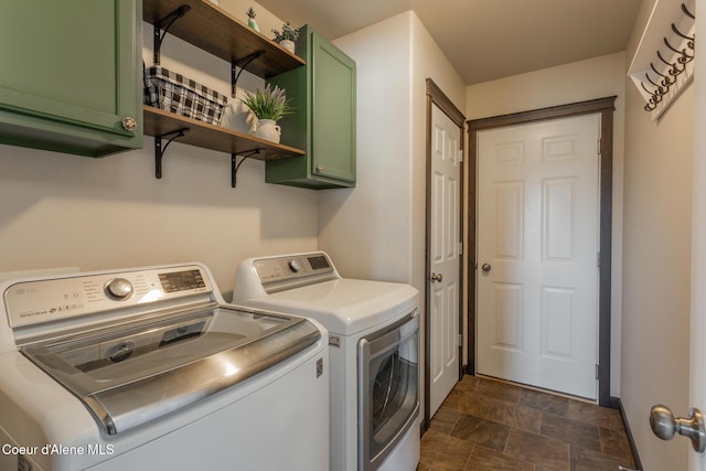 clothes washing area featuring stone finish flooring, washer and clothes dryer, and cabinet space