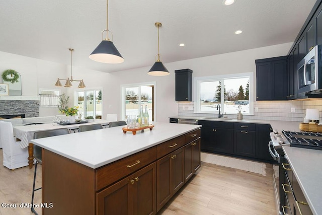 kitchen featuring appliances with stainless steel finishes, a center island, decorative light fixtures, light countertops, and a sink