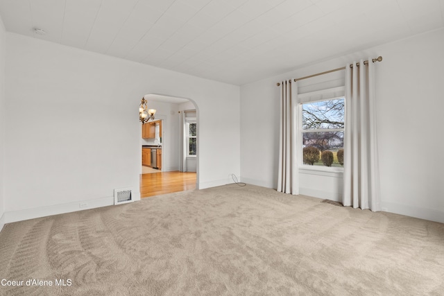 carpeted spare room with an inviting chandelier, arched walkways, visible vents, and baseboards