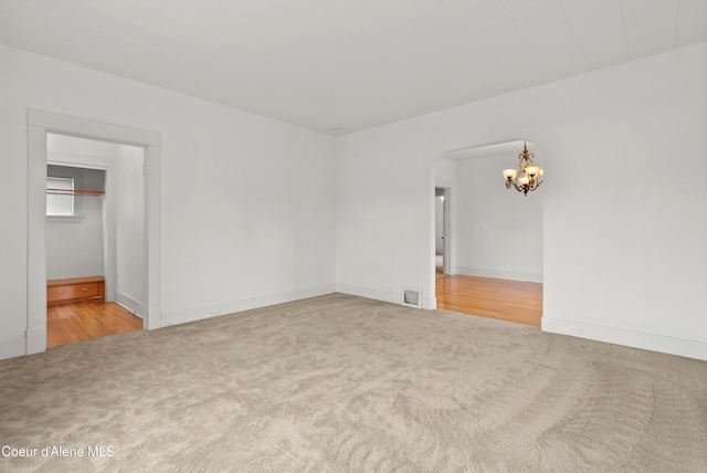 spare room with arched walkways, carpet flooring, visible vents, and an inviting chandelier