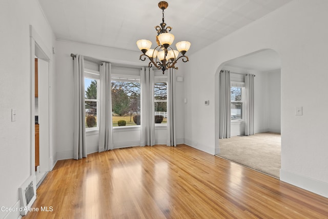 unfurnished dining area with visible vents, baseboards, an inviting chandelier, arched walkways, and light wood-style floors