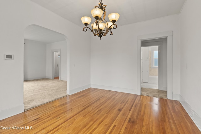 spare room featuring light wood-type flooring, arched walkways, baseboards, and a chandelier