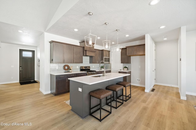 kitchen with appliances with stainless steel finishes, a kitchen island with sink, a sink, and light wood-style flooring