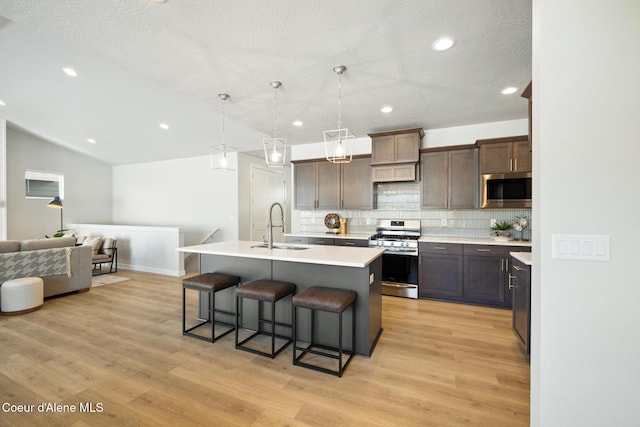 kitchen featuring a sink, light countertops, appliances with stainless steel finishes, tasteful backsplash, and a kitchen bar