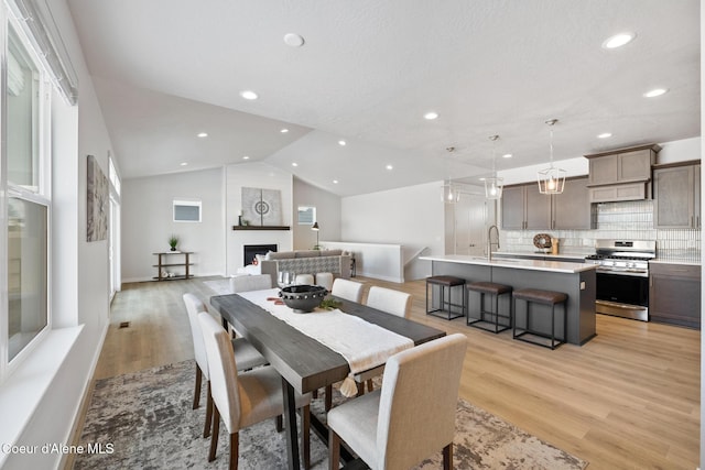 dining space featuring baseboards, vaulted ceiling, light wood-type flooring, a fireplace, and recessed lighting