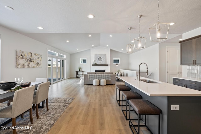 kitchen featuring lofted ceiling, light countertops, light wood-style floors, a fireplace, and a sink