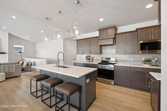 kitchen featuring light wood finished floors, appliances with stainless steel finishes, a kitchen breakfast bar, a sink, and backsplash