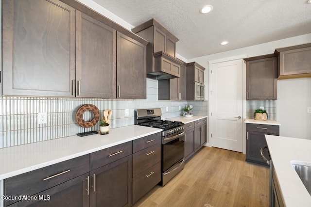 kitchen featuring decorative backsplash, stainless steel range with gas cooktop, light countertops, and light wood finished floors