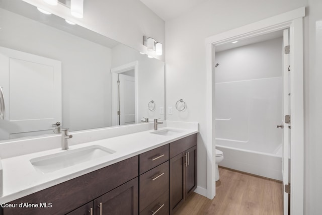 bathroom with toilet, double vanity, a sink, and wood finished floors