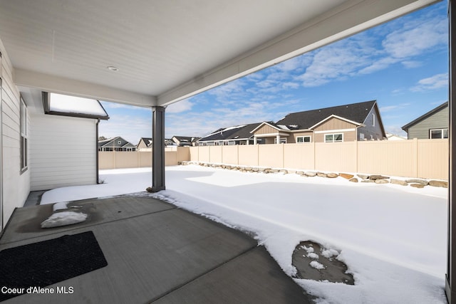 snow covered patio with a fenced backyard and a residential view