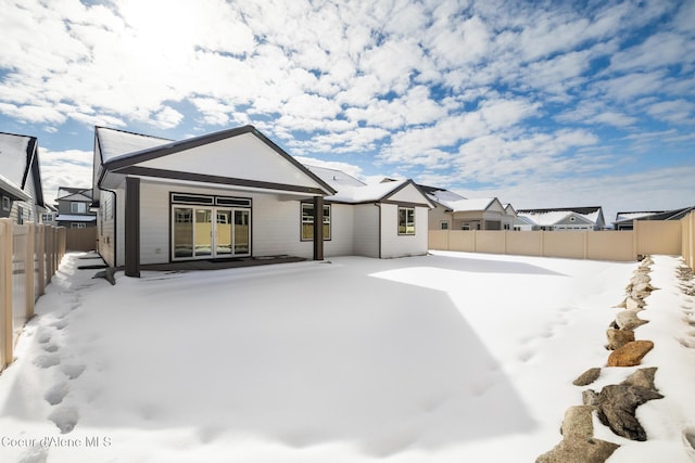 snow covered back of property featuring a fenced backyard