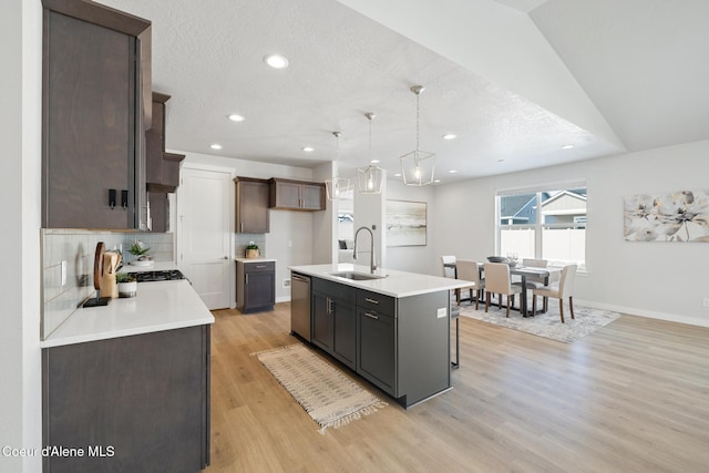 kitchen featuring a kitchen island with sink, light wood-style flooring, a sink, light countertops, and stainless steel dishwasher