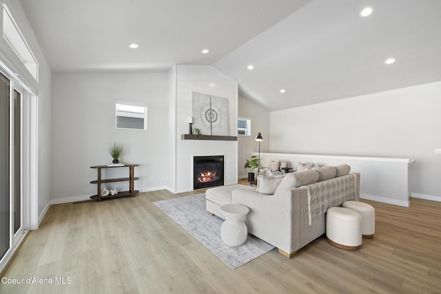 living room featuring vaulted ceiling, a fireplace, light wood-style flooring, and baseboards