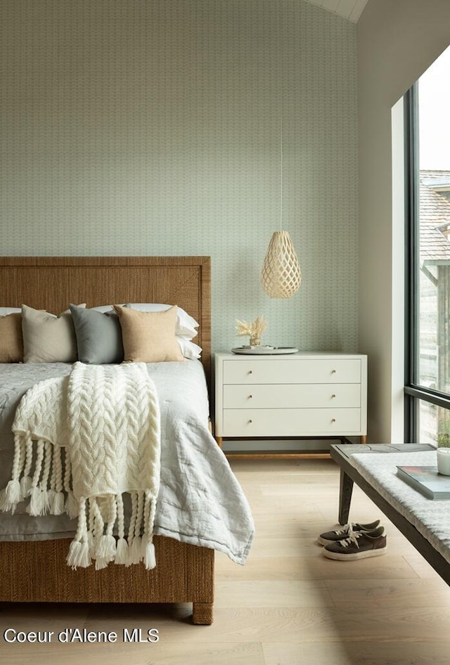 bedroom with light wood finished floors, a wall of windows, and wallpapered walls