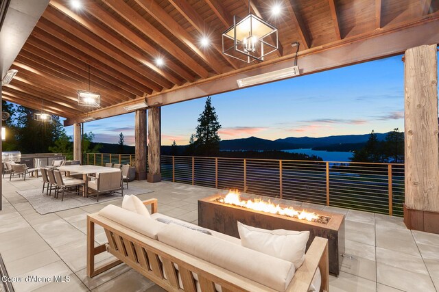 6895 S Gozzer Rd Unit A201, Harrison, ID 83833 - patio terrace at dusk featuring an outdoor living space with a fire pit, outdoor dining space, a patio area, an outdoor kitchen, and a mountain view