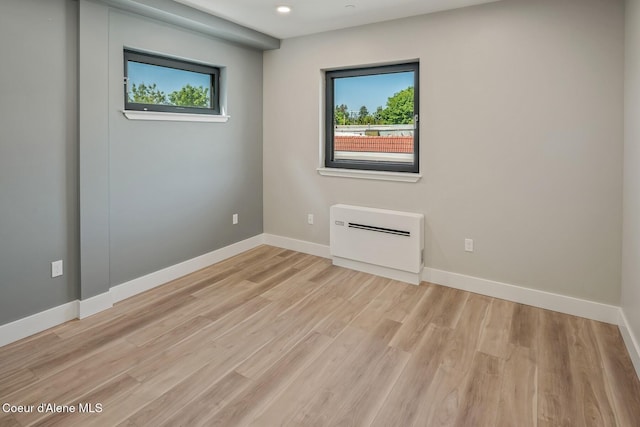 unfurnished room with baseboards, an AC wall unit, light wood-style floors, and a healthy amount of sunlight