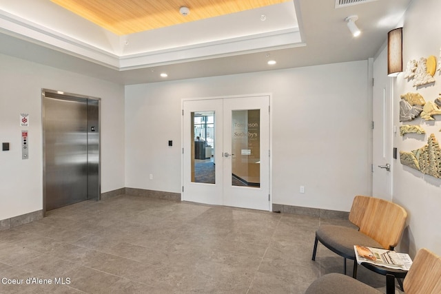 interior space featuring elevator, baseboards, a tray ceiling, and french doors